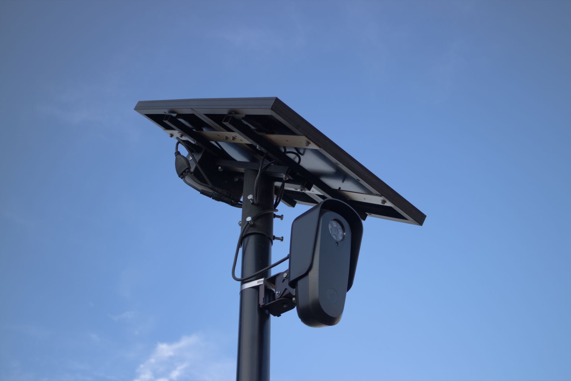 Solar-powered Flock Safety license plate reader camera mounted on a roadside pole against a blue sky.